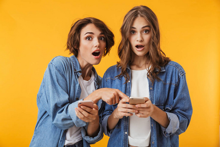 照片的震惊情绪年轻女性朋友冒充在黄色背景下使用手机