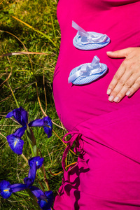 孕妇与婴儿鞋在她的肚子上躺在草地上