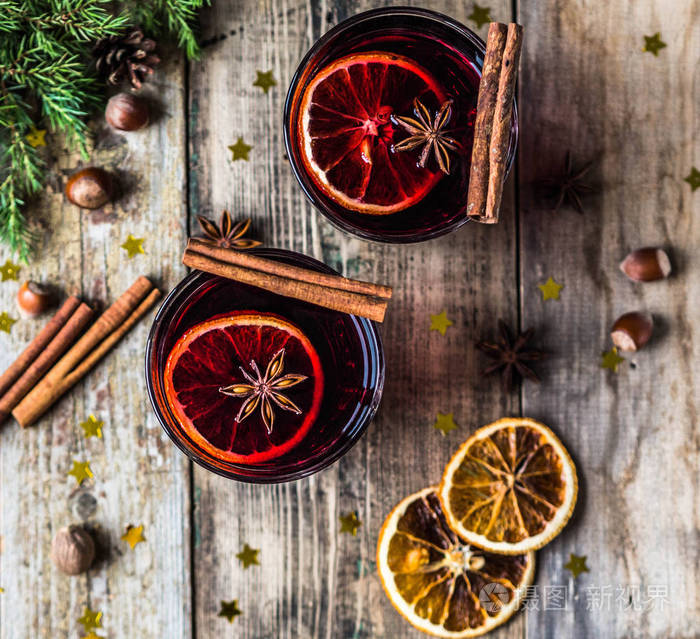 传统的冬季酒精饮料美酒。热葡萄酒与水果和香料在玻璃在老木背景