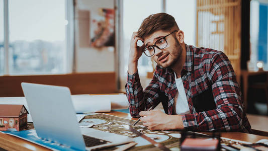 坐在办公桌工程项目的人的肖像。年轻的胡子平面设计师画师穿着眼镜坐在桌子上专注于笔记本电脑屏幕。创意工作理念