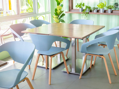 现代蓝色椅子和木桌近窗玻璃和植物装饰在浅绿色船集装箱墙上。简约咖啡厅内饰