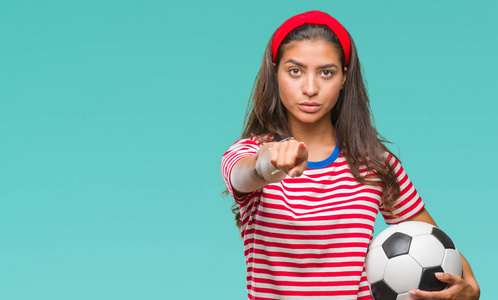 年轻美丽的阿拉伯妇女举行足球足球在孤立的背景下指向相机和你, 手势, 正面和自信的手势从前面