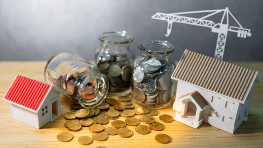 房子和起重机模型与硬币在货币玻璃罐子在木桌上。房屋按揭贷款利率。省钱。房地产开发或物业投资。建筑行业经营理念