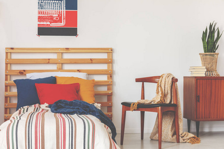 蓝色,红色和橙色枕头在单人床上,有的羽绒被和木制床头板在老学校的卧室内部,真正的照片