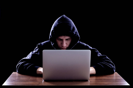 黑客在帽衫坐在笔记本前的黑暗图片
