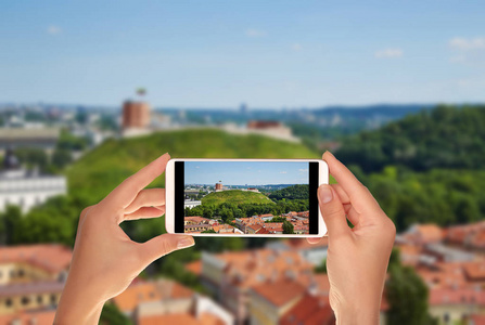 一名游客正在用手机拍摄维尔纽斯全景照片, 在夏日阳光明媚的日子里, 可以看到城堡山的景色