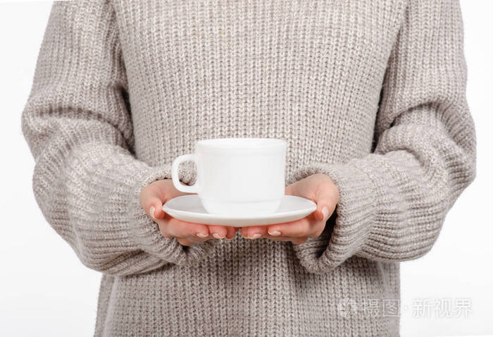 穿着毛衣的年轻女子手里拿着一个白色的杯子和茶托, 喝着热咖啡