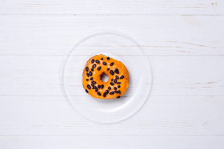 在白色木桌上的透明玻璃板上涂上奶油的釉红色橙色甜甜圈, 顶视图