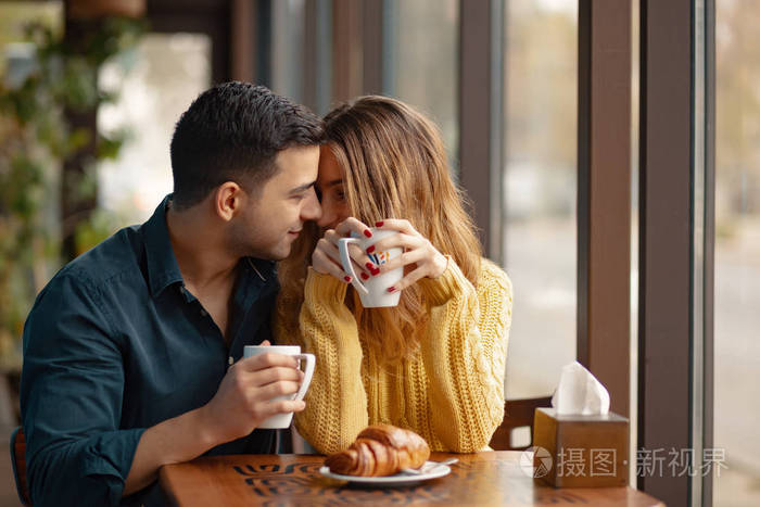 年轻的夫妇约会在咖啡店.恋爱中的男人和女人坐在咖啡馆里 喝着咖啡