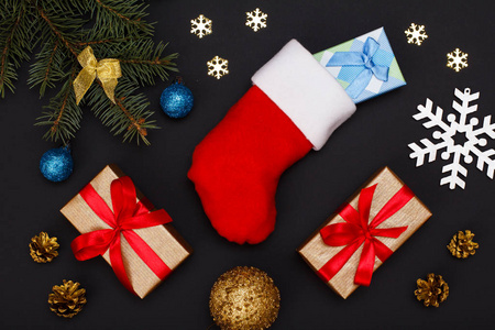 圣诞装饰。圣诞老人的靴子, 礼品盒, 天然冷杉树枝与锥和圣诞玩具在黑色的背景。顶部视图。圣诞贺卡概念