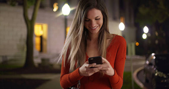 千禧一代的女人在智能手机上发短信, 晚上在外面看起来很开心