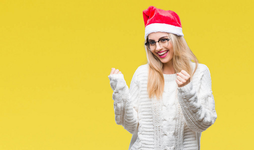 年轻美丽的金发女子戴着圣诞节帽子在孤立的背景非常高兴和兴奋做赢家手势与手臂举起, 微笑和尖叫的成功。庆典理念