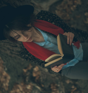 手里拿着书的年轻女子坐在树干旁边, 在黄昏的时候看书。顶视图
