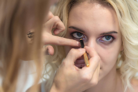 化妆与画笔在一个美丽的金发女郎的脸上与阴影的模型的眼睛