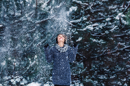 在冬季森林的毛衣时尚开朗的女孩。树上的雪落在女孩身上