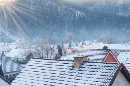 在一个下雪的村庄的霜晨.在住宅的屋顶上抽烟.加热煤和木材照片