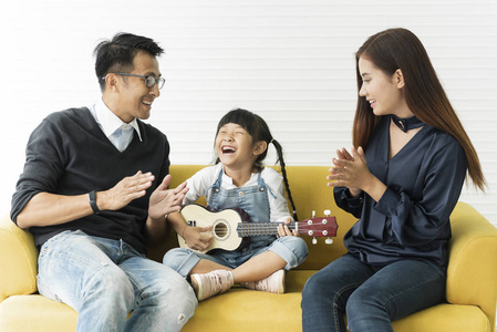 亚洲女儿在客厅的沙发上弹吉他, 和爸爸妈妈一起唱歌。概念家庭享受