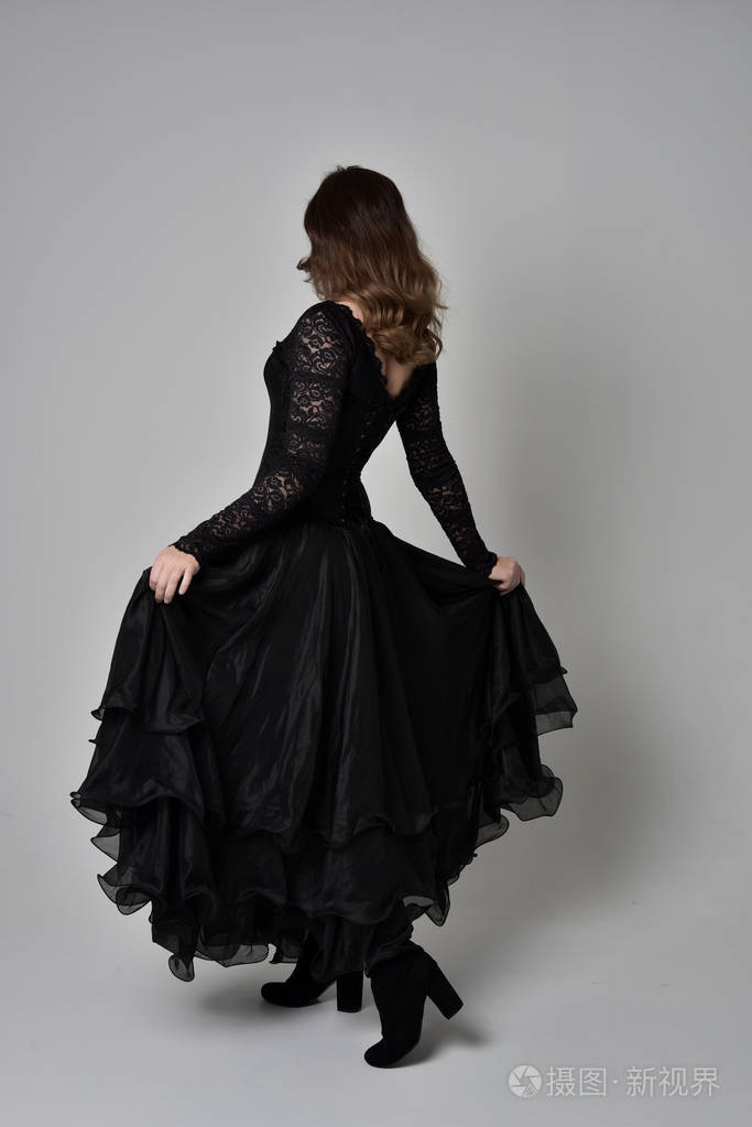 黑发女孩穿着黑色长袍的全长肖像机智紧身胸衣.站在镜头前摆姿势.