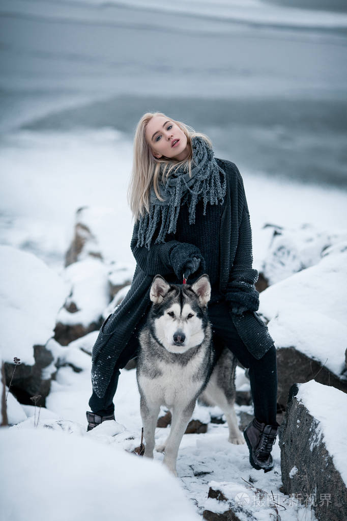 与狗阿拉斯加雪橇犬在冬天在岩石中的女孩