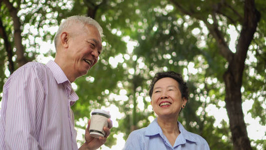 愉快的亚洲老人夫妇早晨散步在绿色城市喝咖啡和谈话