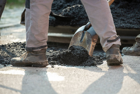 用铲子修补街道上的碰撞的工人用铲子布置新鲜沥青混合料的低角度视角