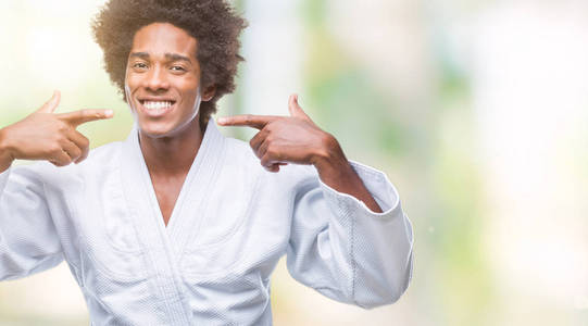美国黑人男子身穿空手道和服在孤立的背景下微笑着自信地显示和指着手指的牙齿和嘴巴。健康理念