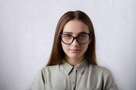 美丽自信的女孩，穿着大 glassses 看着相机在灰色的背景中分离的长直发一幅画像。一个聪明的学生戴眼镜。学习和教育的概念