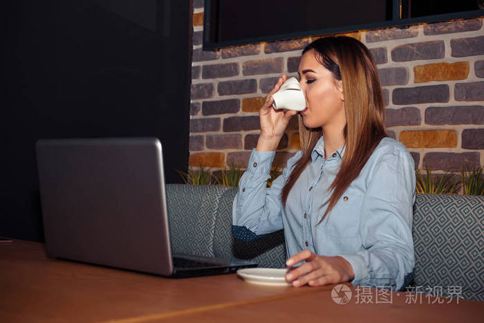 企业家与笔记本电脑放松, 同时喝咖啡和微笑, 而坐在一个现代化的咖啡馆内部