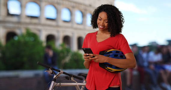 愉快的黑人妇女游客在罗马停留在斗兽场发送短信在电话