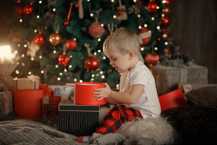 愉快的小微笑的男孩在红色睡衣与圣诞礼物箱子在客厅在家居装饰