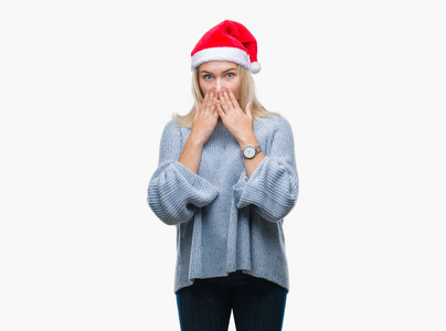年轻的白种女人戴着圣诞帽子在孤立的背景下震惊地用手捂住嘴巴。秘密概念