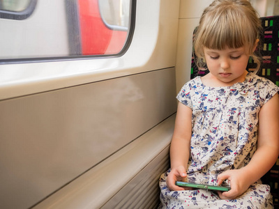 可爱的高加索小女孩坐在火车车厢里玩手机