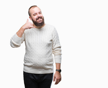 年轻的高加索嬉皮士男子穿着冬季毛衣在孤立的背景微笑着做电话手势用手和手指喜欢在电话里说话。传达概念