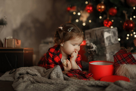 愉快的小微笑的女孩在红色睡衣与圣诞礼物箱子在客厅在家居装饰