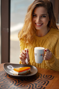 漂亮的年轻女子享受一杯咖啡和一片美味的蛋糕, 而休息, 阳光透过窗户在咖啡馆里闪耀