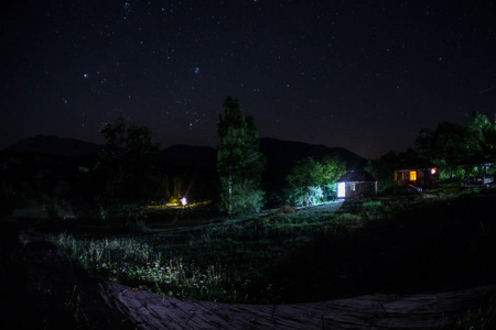 晚上在森林里建筑的山夜风景与月亮或老式乡下房子在晚上与云彩和星。夏日之夜。照片拍摄与长期曝光