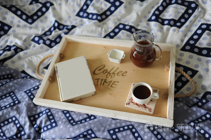 躺在床上吃早餐。这本书，一壶，一杯咖啡手工木制托盘上。蓝色亚麻