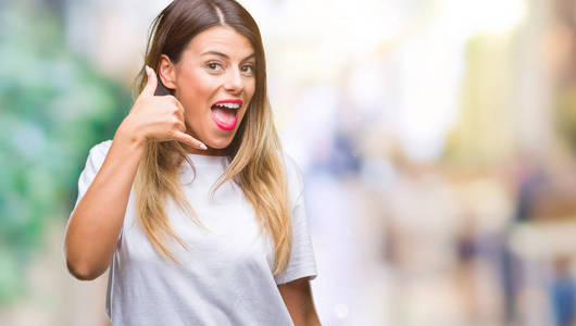 年轻美丽的妇女休闲白色 t恤在孤立的背景微笑做电话手势用手和手指喜欢说话的电话。沟通概念