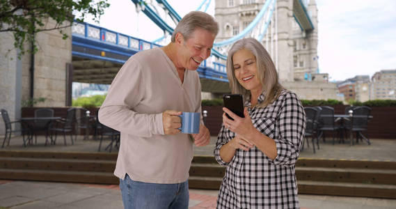 成熟的高加索丈夫和妻子看在塔桥附近的电话照片