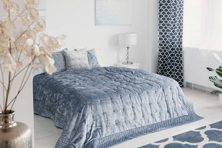 白色优雅卧室内的花朵, 床头有蓝色床单, 旁边是台灯和窗帘。真实照片