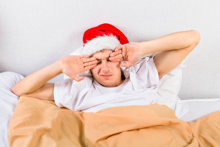 疲惫的年轻人在圣诞老人的帽子在家里的床上