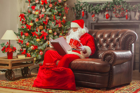 圣诞老人坐在他的家, 在一个舒适的椅子和阅读