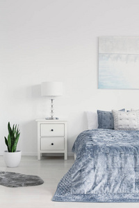 卧室的垂直视图与大舒适的床, 蓝色床上用品, 白色床边桌和绿色植物在锅里, 真实的照片与复制空间