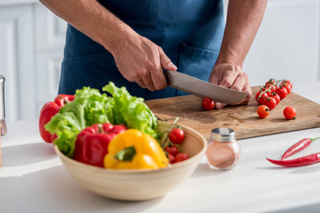 部分视图的人切割樱桃西红柿在切菜板上的厨房