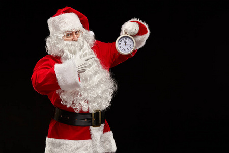 在黑色背景上的圣诞老人指着他的手指在时钟。圣诞节的概念。新年理念