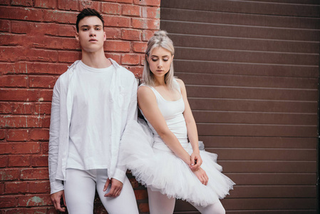一对年轻的舞者在白色的衣服站在一起附近砖墙街道