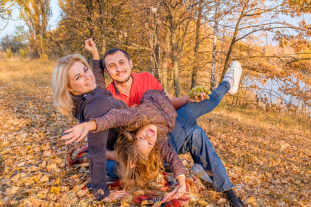 胡子的父亲拥抱他的妻子和女儿。年轻的微笑的家庭坐在秋草上, 在格子上玩得很开心。幸福家庭和无忧无虑的童年的概念