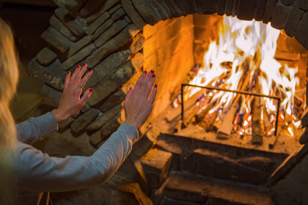 冬日房间金发碧眼的女孩在壁炉里的炉火旁温暖着她的双手.