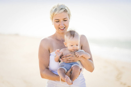 有吸引力的金发妈妈玩与4月大男婴在海滩上