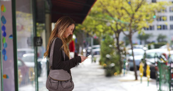 千禧一代女孩在市中心的手机上在餐馆外等候短信